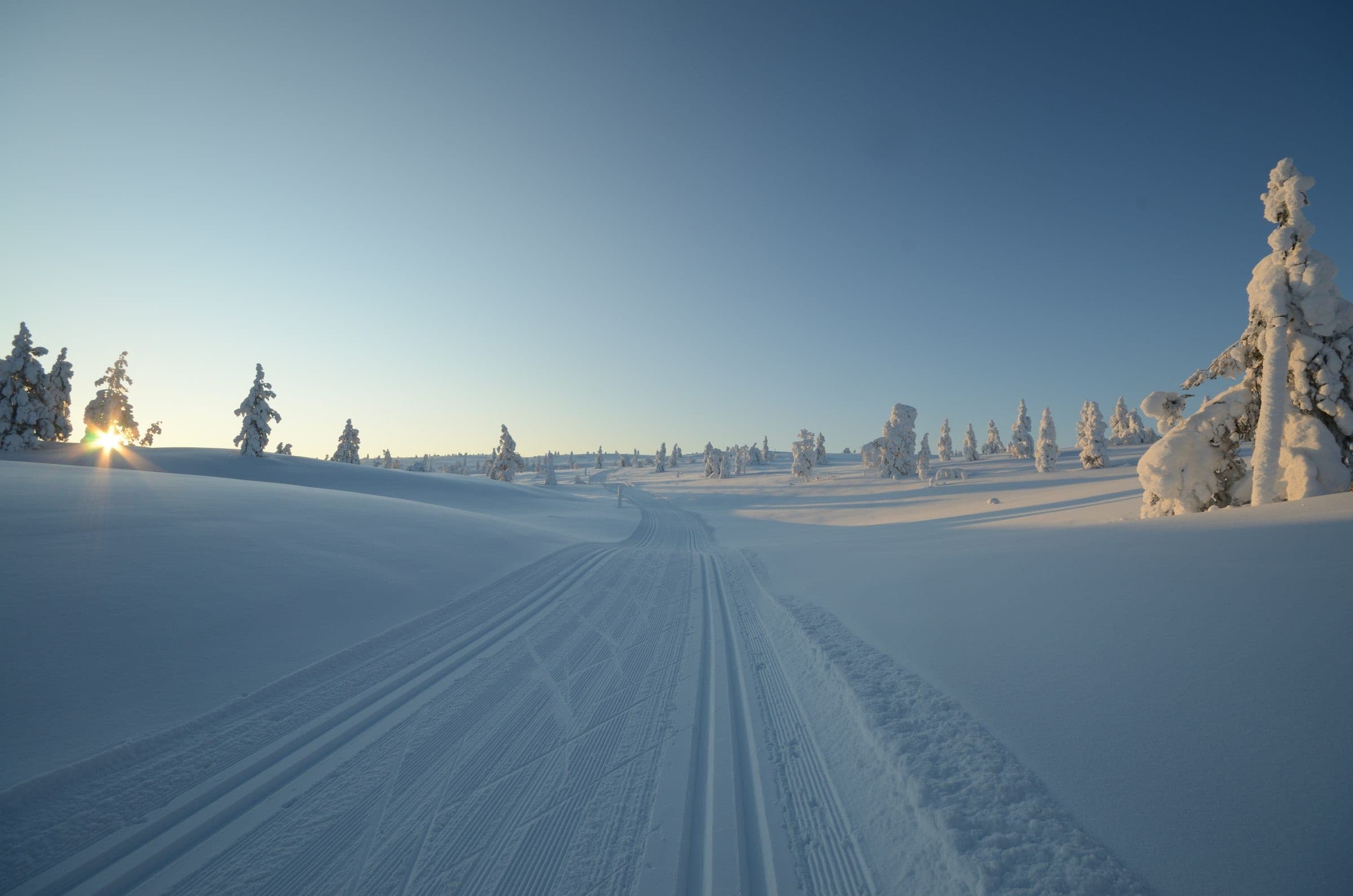 A groomed trail running through snow-covered fells towards a low sun